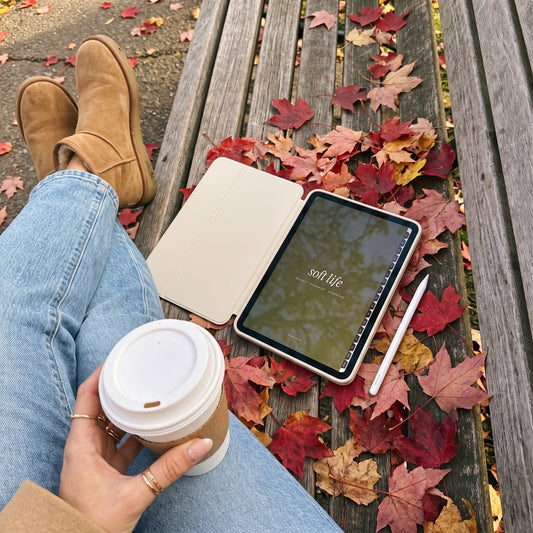 Soft Life budget planner on an iPad on a park bench with fall leaves and a coffee