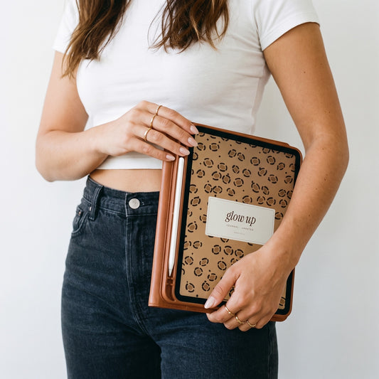 Woman in a white tee holding an iPad with the Glow-Up Journal leopard cover at her hip