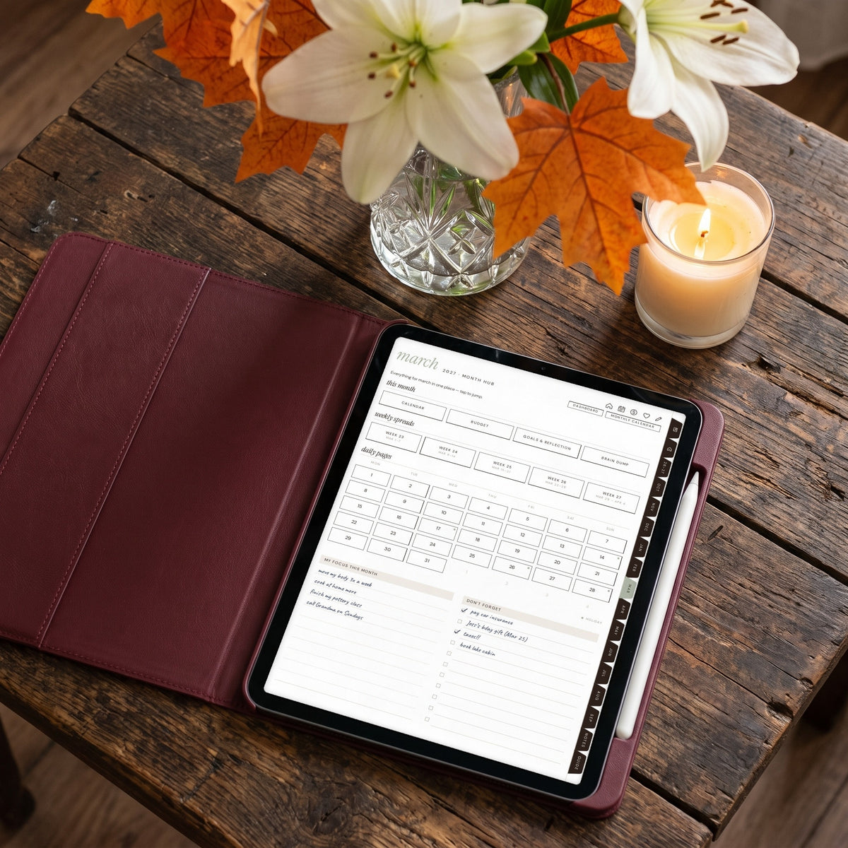 2026-2027 Weeklie month hub page on an iPad in a burgundy case beside lilies