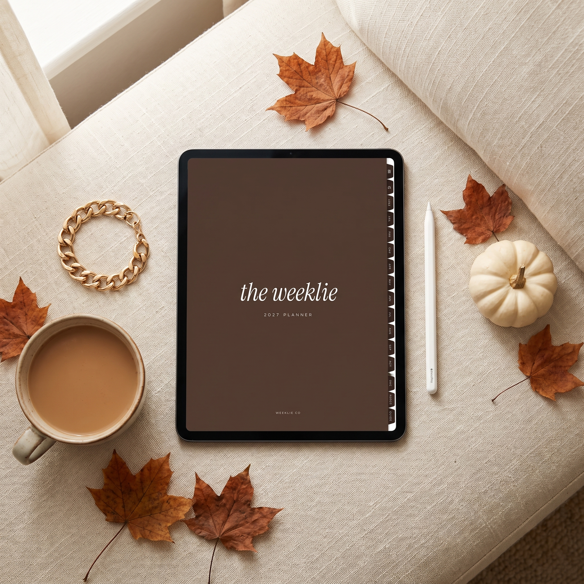 The 2027 Weeklie digital planner cocoa cover on an iPad in a fall flat lay with chai and maple leaves