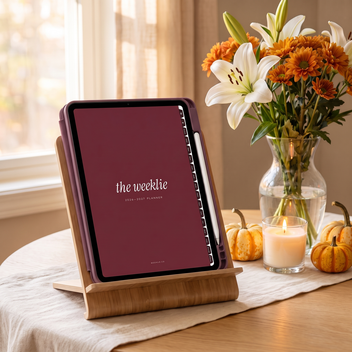iPad in a plum case on a wood stand showing the 2026-2027 planner cover with lilies