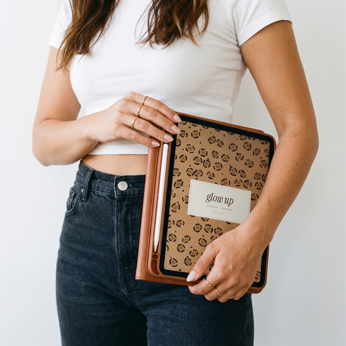 Woman in a white tee holding an iPad with the Glow-Up Journal leopard cover at her hip